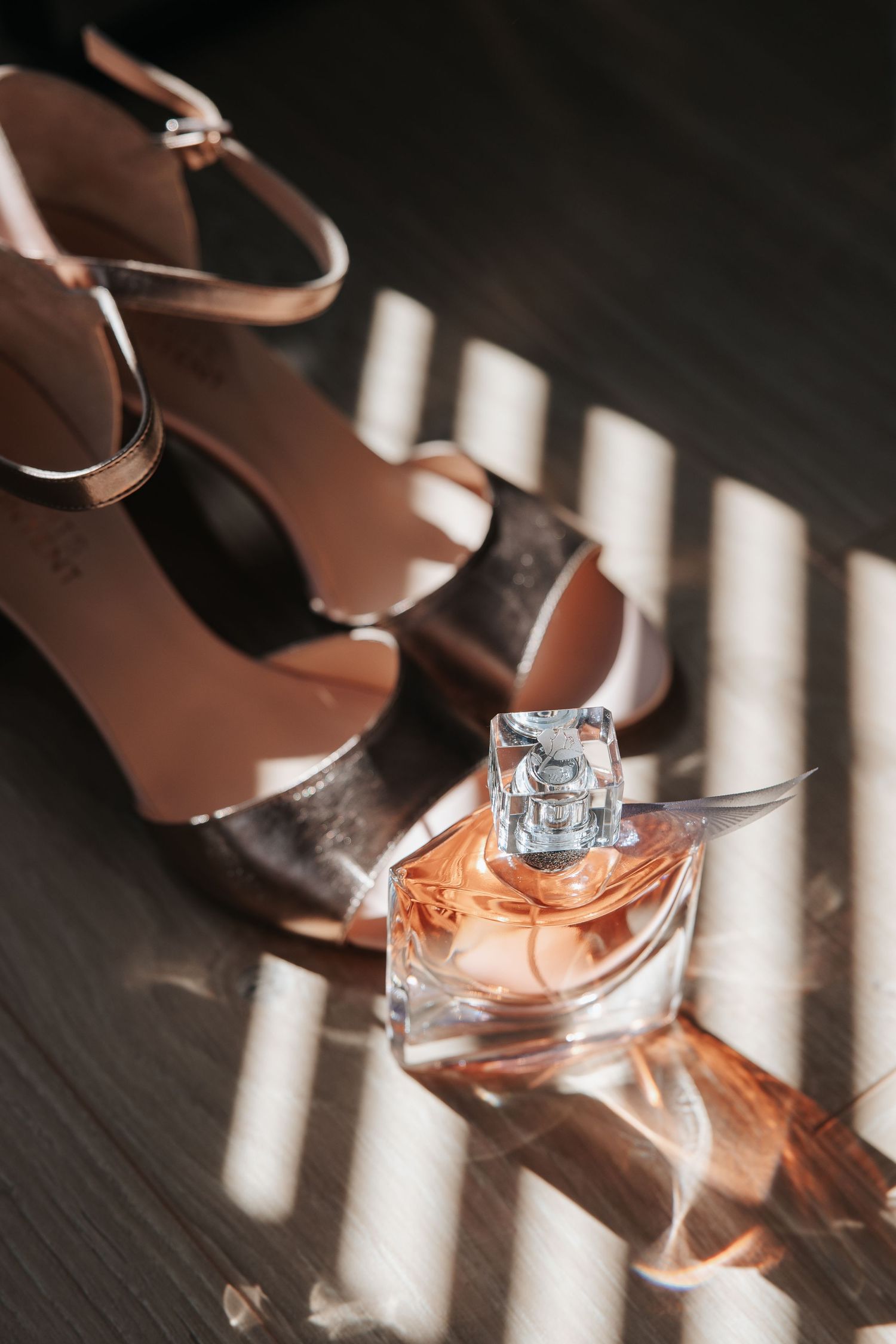 Stylish wedding accessories with perfume bottle and heels casting dramatic shadows.