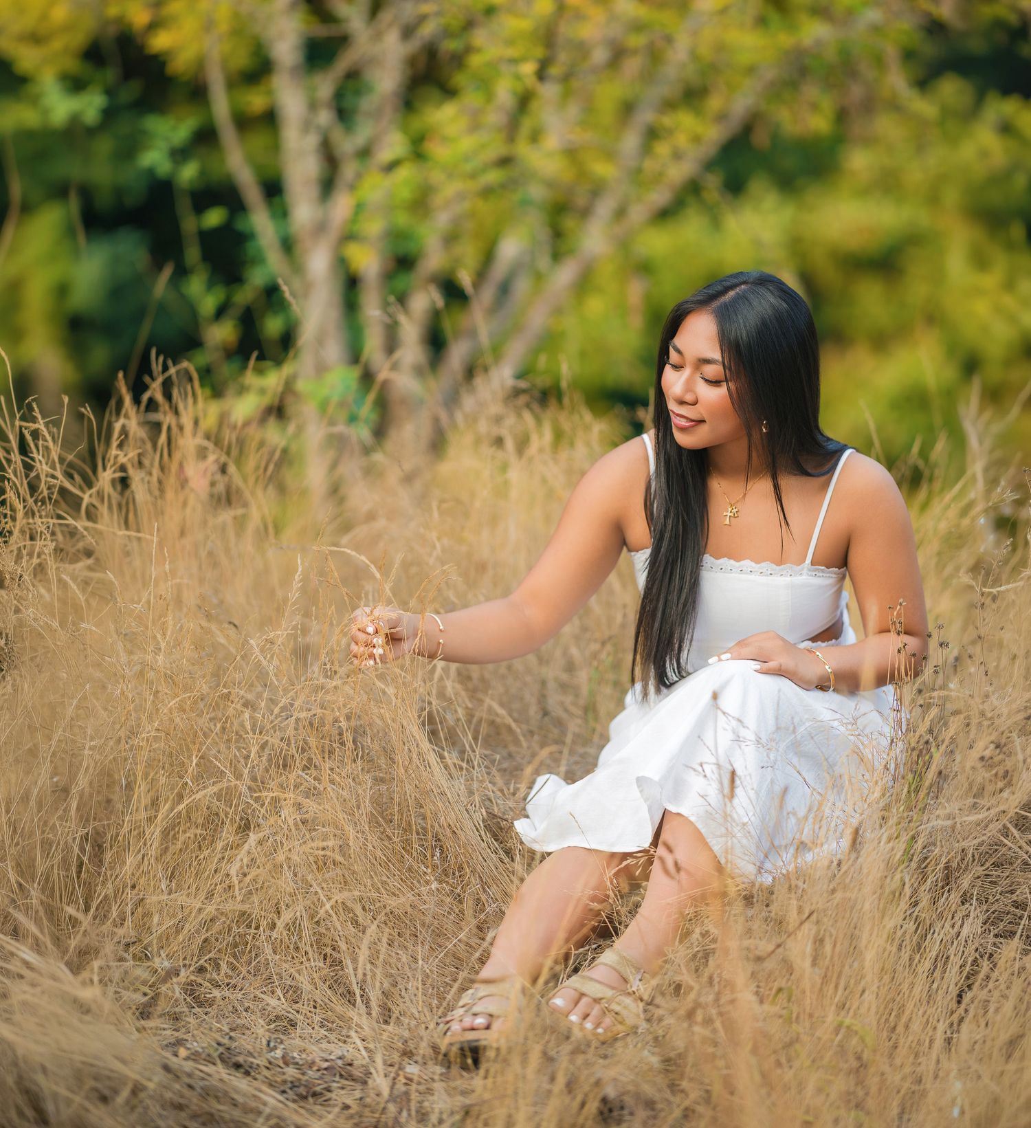 Young woman in white dress sitting among golden tall grass in a natural outdoor field setting.