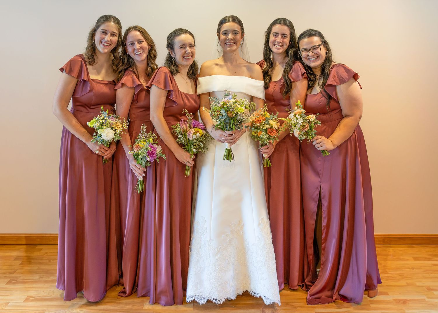 A bride and bridesmaids standing and smiling before the Sacrament of Holy Matrimony at a Catholic church.