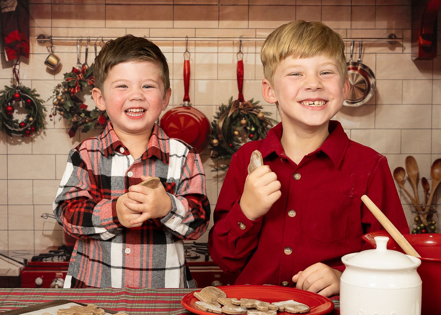 Two smiling boys in red shirts baking Christmas cookies in a festive holiday kitchen.