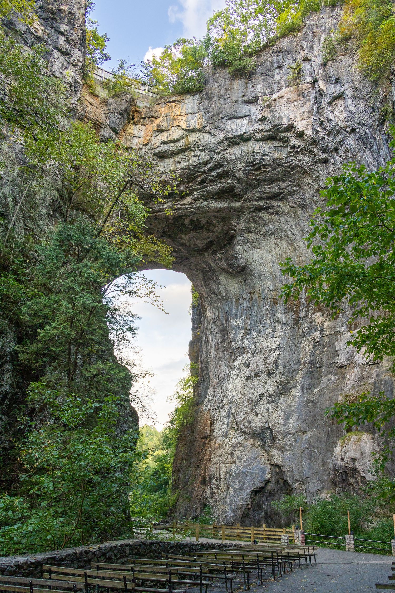 Natural Bridge State Park Virginia, massive limestone arch formation surrounded by lush green trees with outdoor seating below.