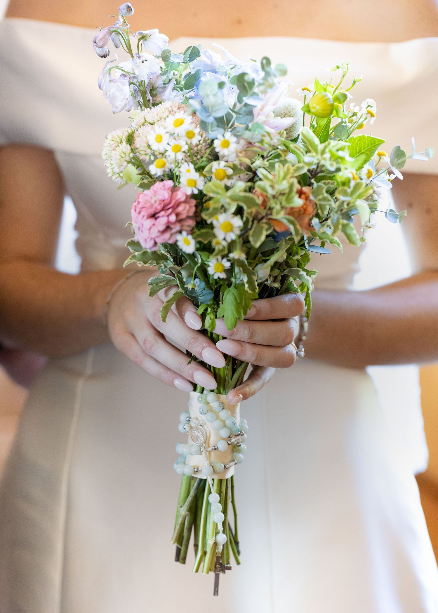 A close-up details photo of a bride's rosary wrapped around her wedding bouquet during a church ceremony.