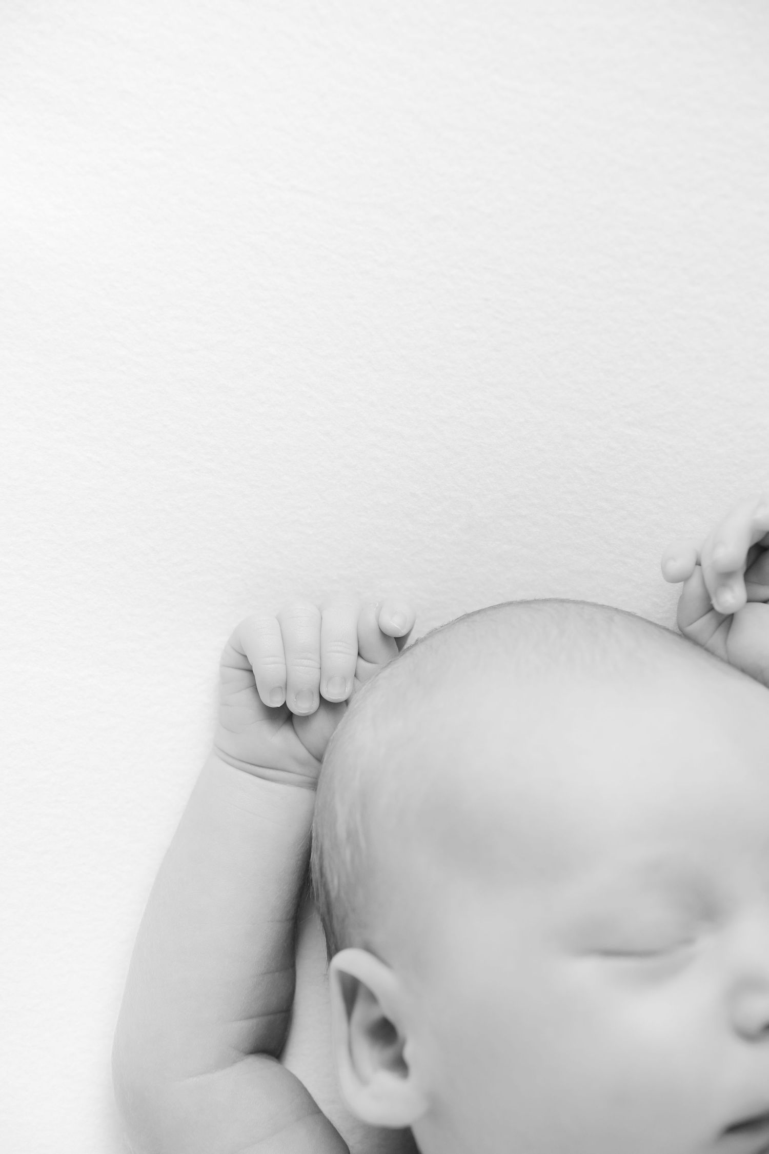 Black and white photo of a sleeping newborn baby with tiny hands near head.
