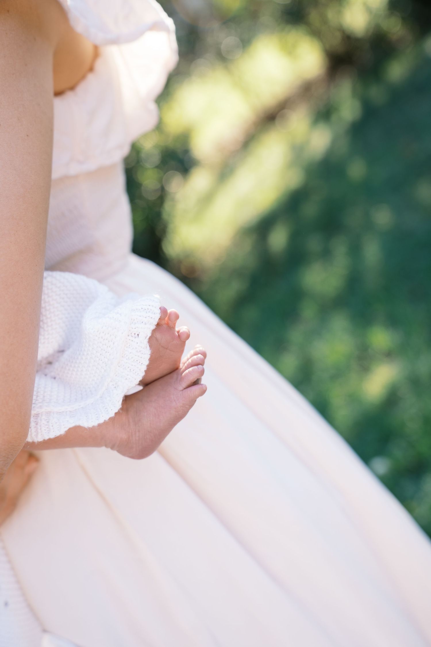 Close-up of tiny newborn baby feet peeking out from a white knit blanket outdoors.