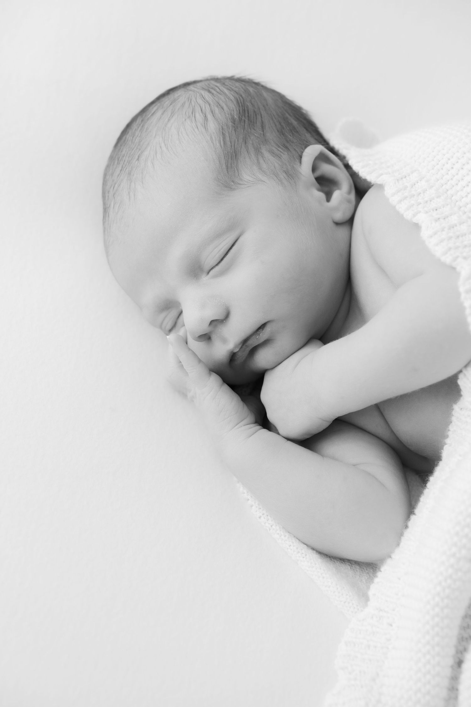 Black and white portrait of a peaceful sleeping newborn baby resting on soft white blanket.