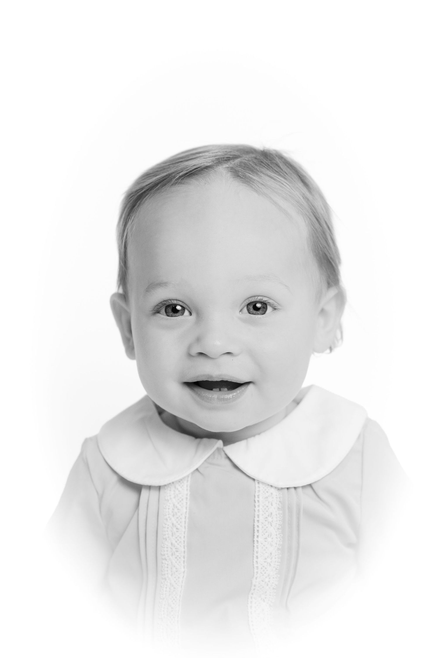 Smiling baby boy in white Peter Pan collar shirt, black and white studio portrait.