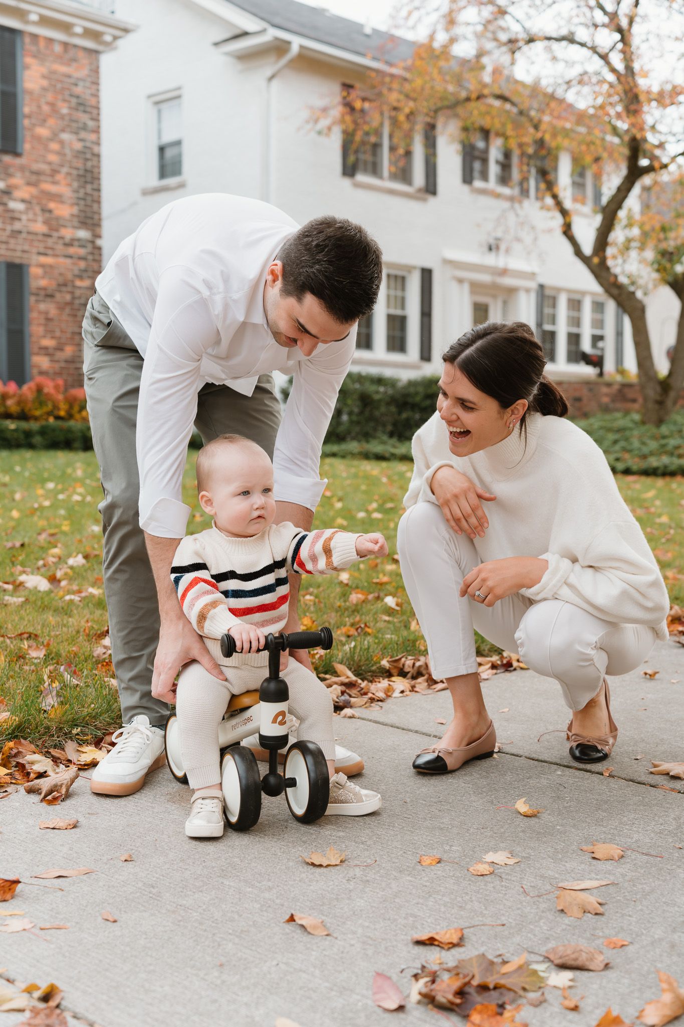 Young west Michigan family with baby on tricycle enjoying autumn day outside suburban home.