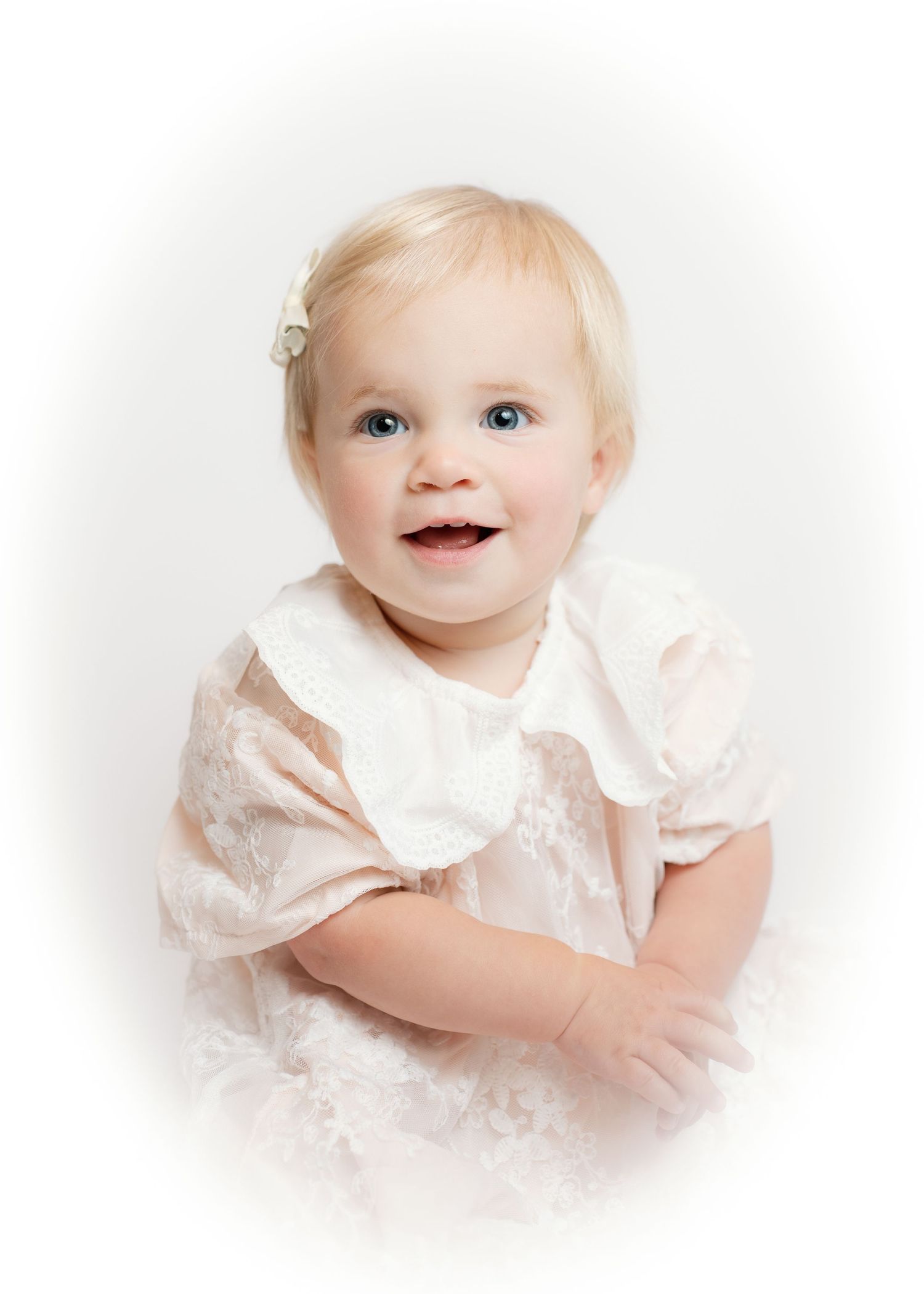Happy blonde baby girl with blue eyes in lace dress, soft vignette studio portrait.