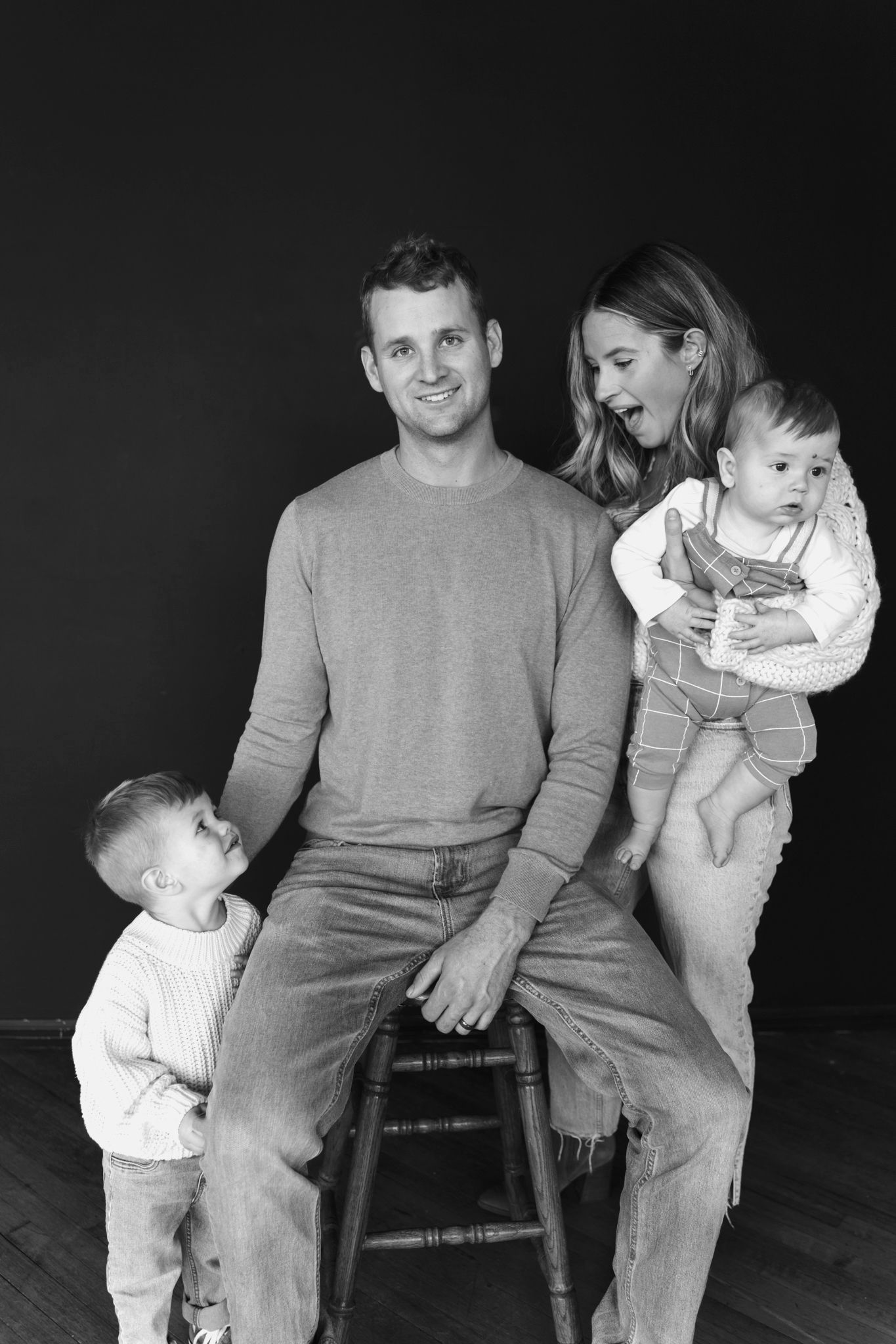 Black and white family portrait with parents and two young children in studio.