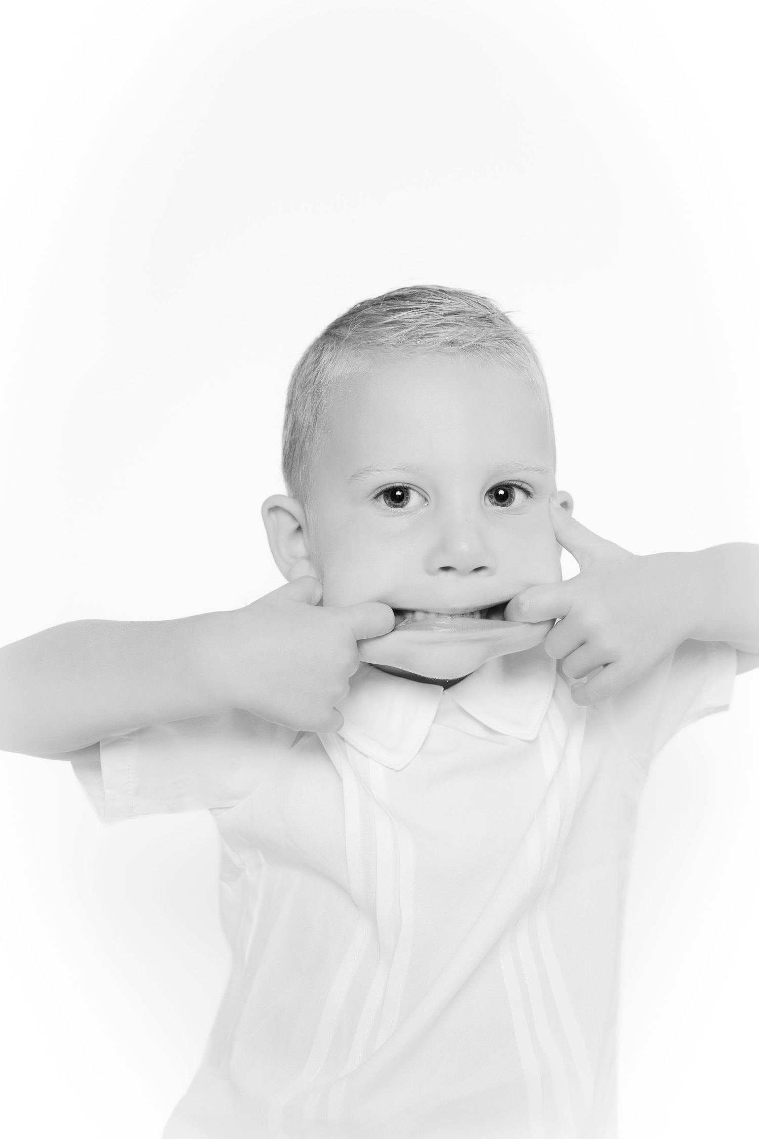 Black and white personality portrait in Grand Rapids, Michigan of a boy pulling a funny face by stretching his mouth wide with his fingers.