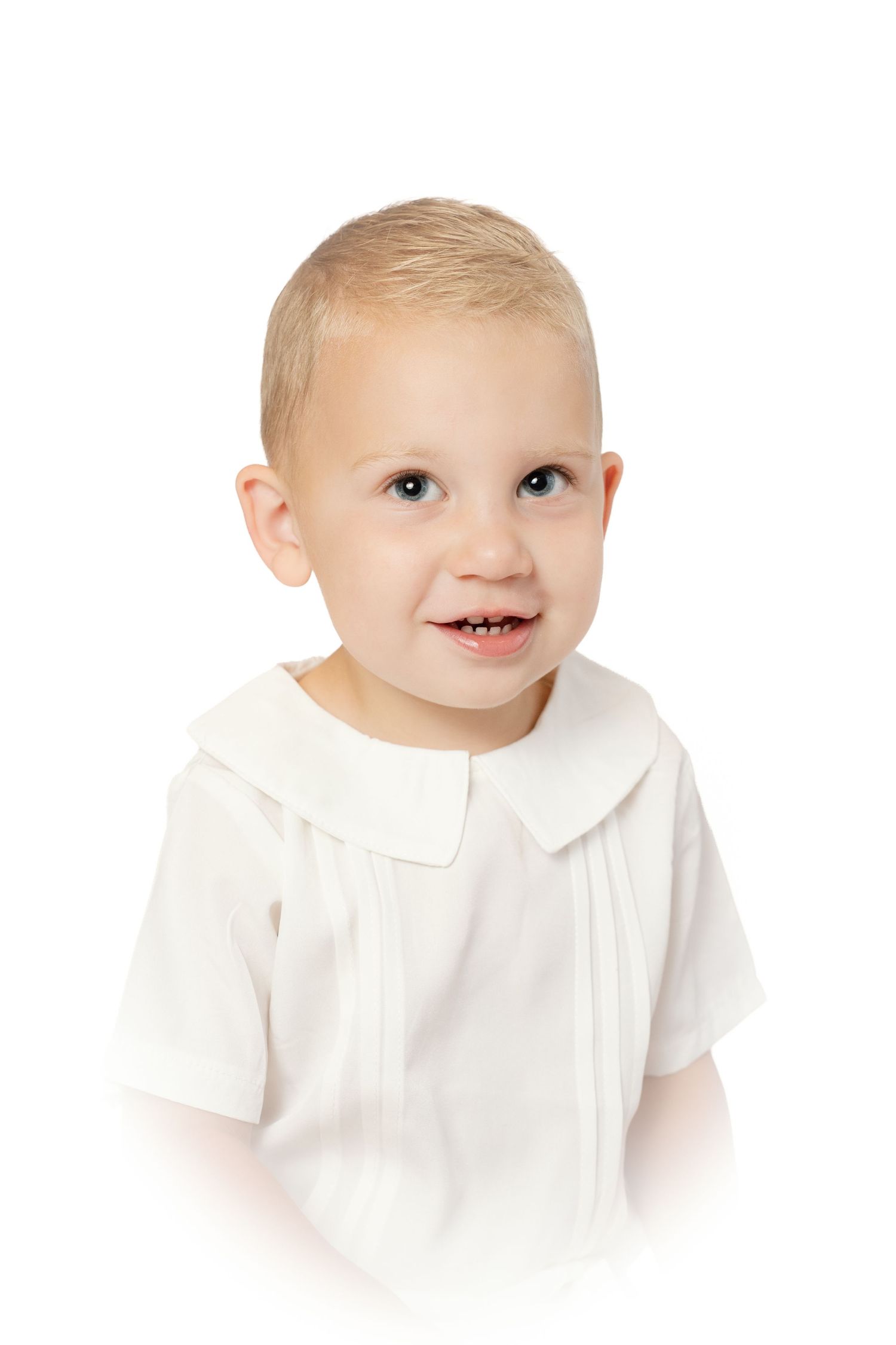 Cheerful blonde toddler boy in a white pleated Peter Pan collar shirt smiling.