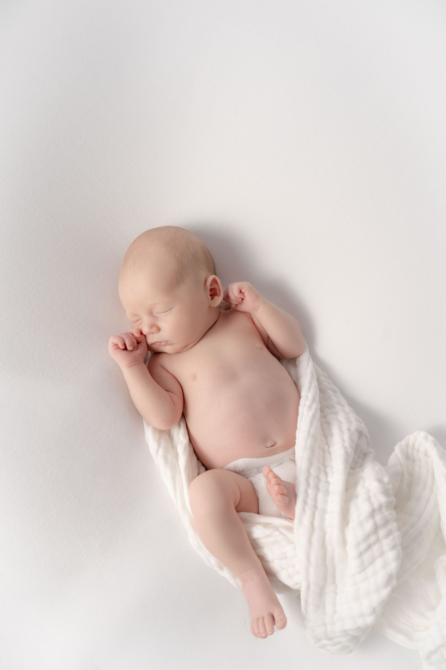 Peaceful newborn baby sleeping on white blanket, soft natural light, photographed in Rockford, Michigan studio