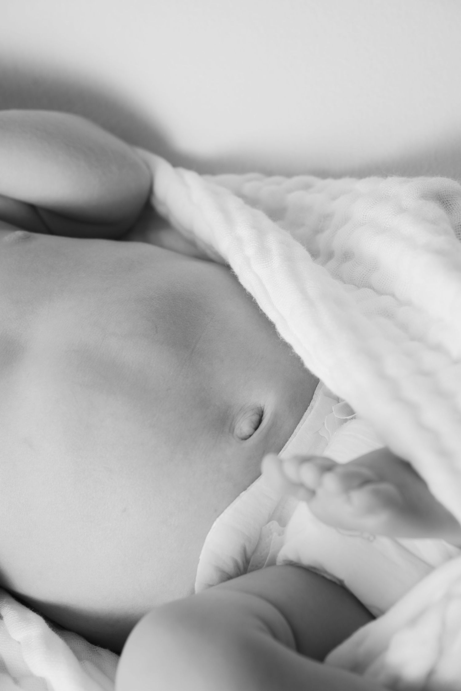 Black and white close-up of a sleeping newborn baby's belly wrapped in a soft white blanket.