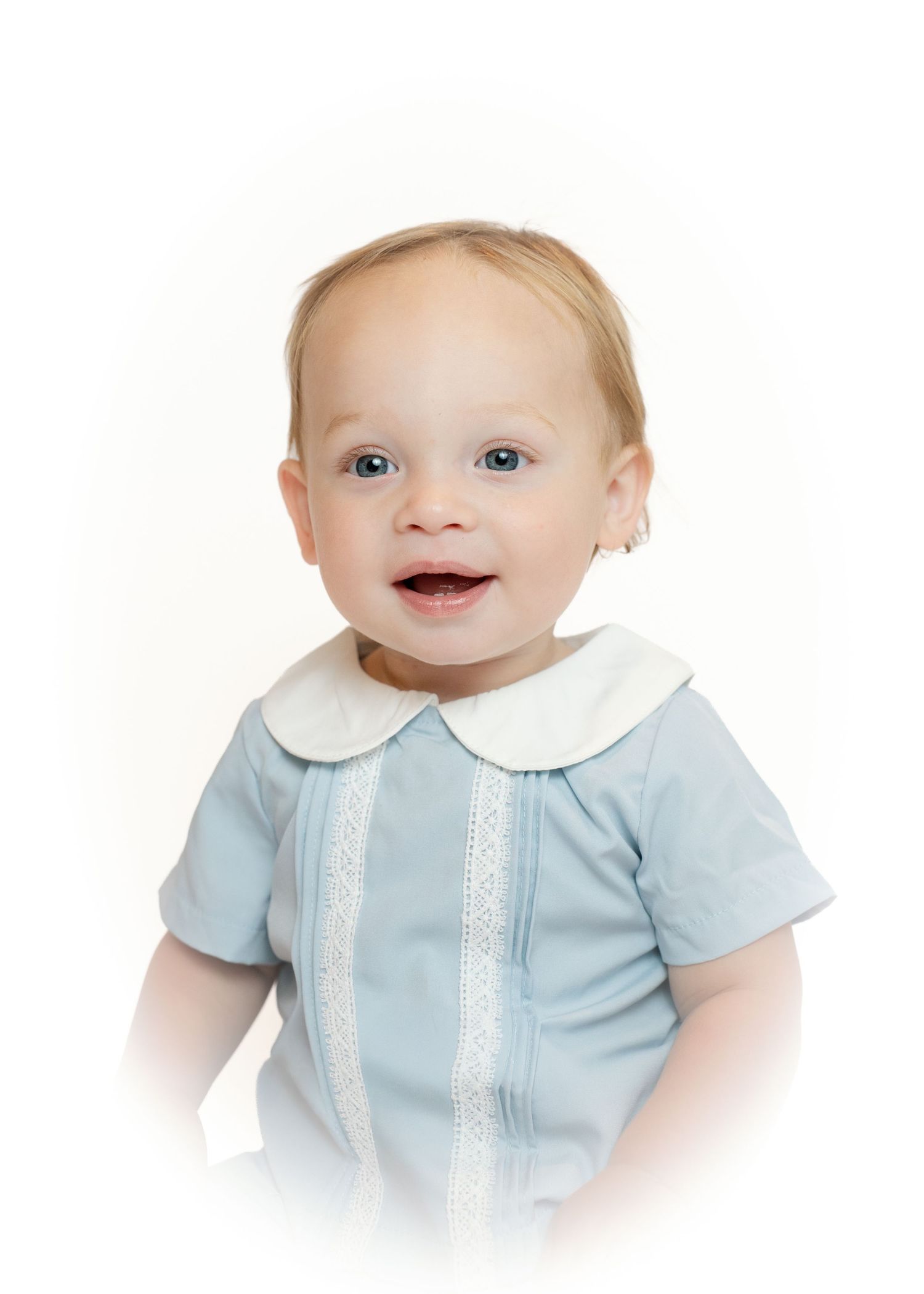 Smiling baby girl with blue eyes wearing a light blue Peter Pan collar outfit, studio portrait.