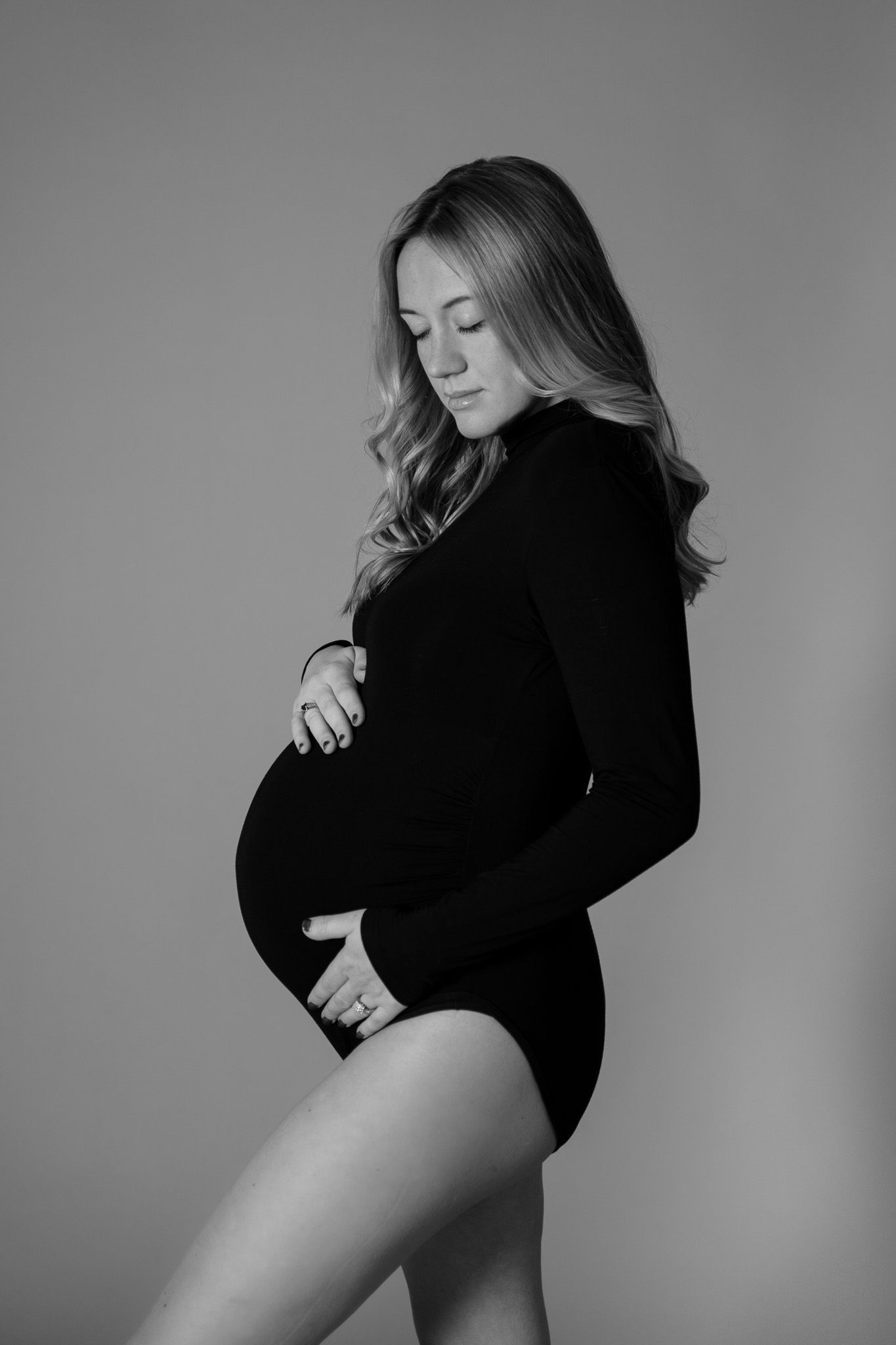 Black and white portrait of a pregnant woman in a black bodysuit cradling her bump.