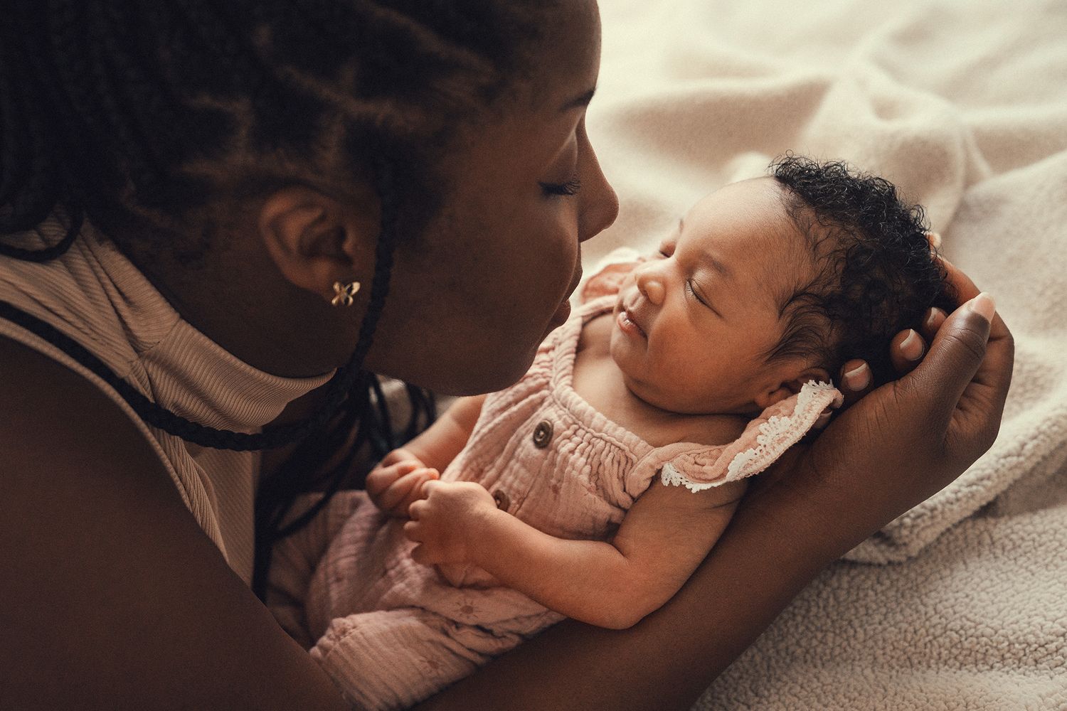 A loving mother gazes tenderly at her sleeping newborn baby girl in a warm, intimate portrait.