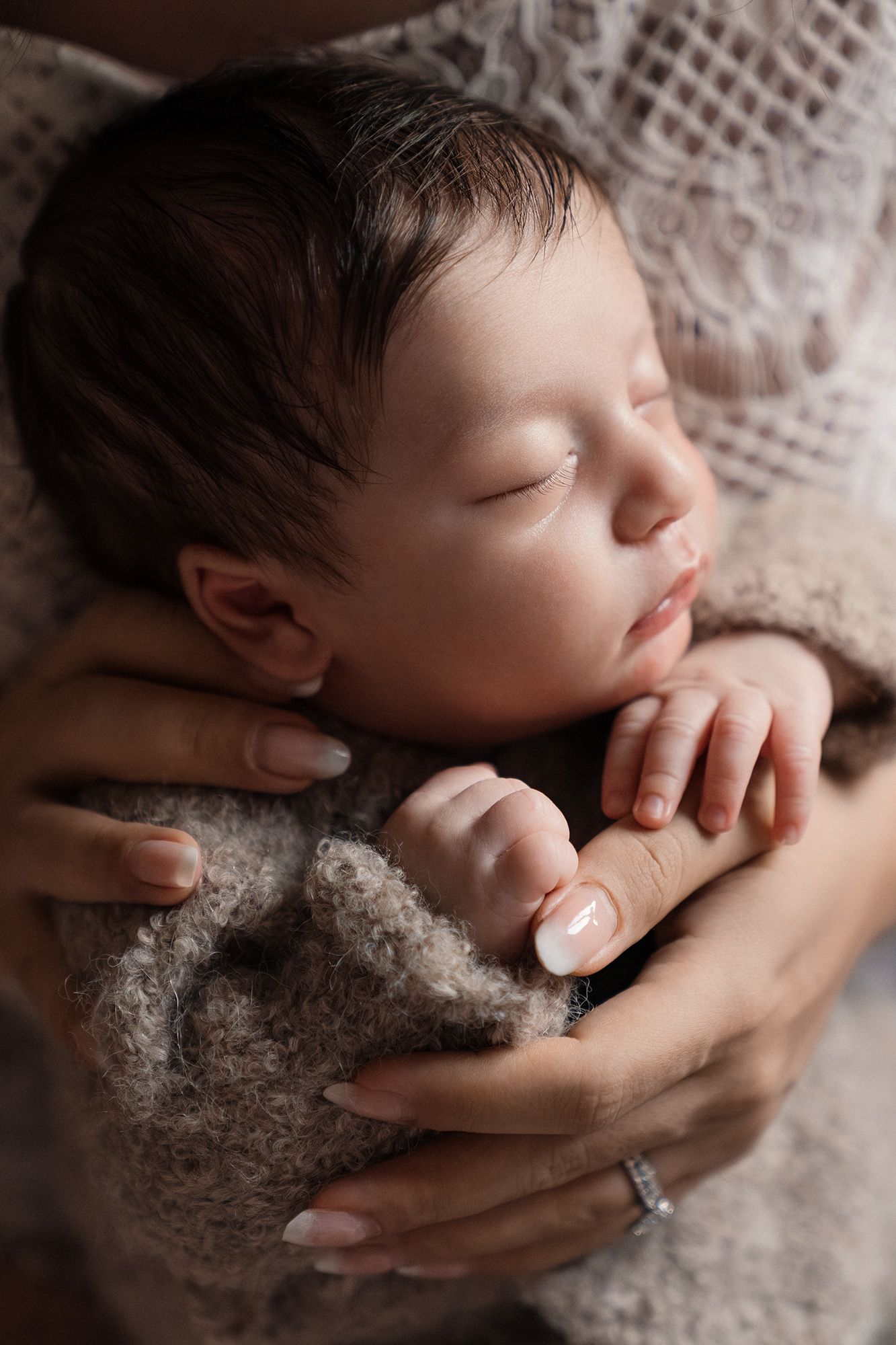 Close-up of a sleeping newborn baby held gently in mothers hands wearing a ring.
