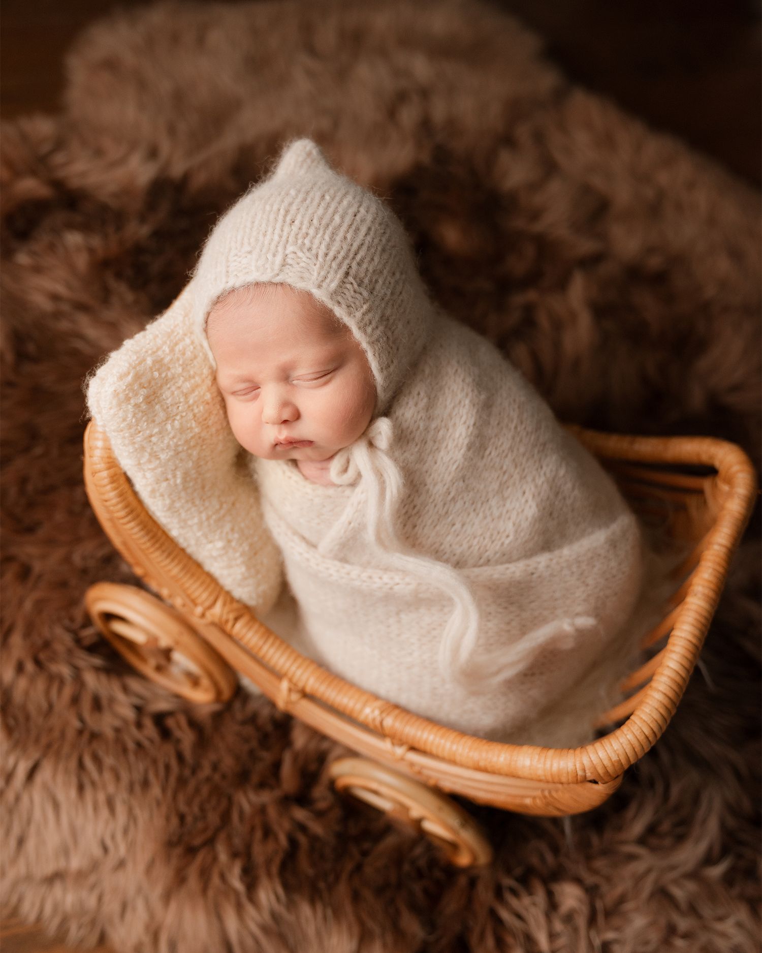 Sleeping newborn in cream knit bonnet and wrap inside wicker pram.