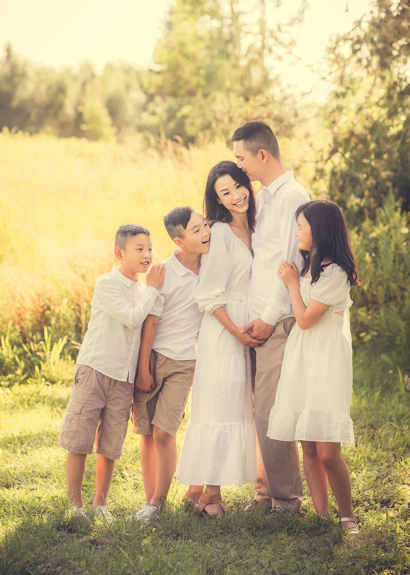 Happy Asian family of five posing together in a sunny meadow, wearing coordinated white and beige outfits.