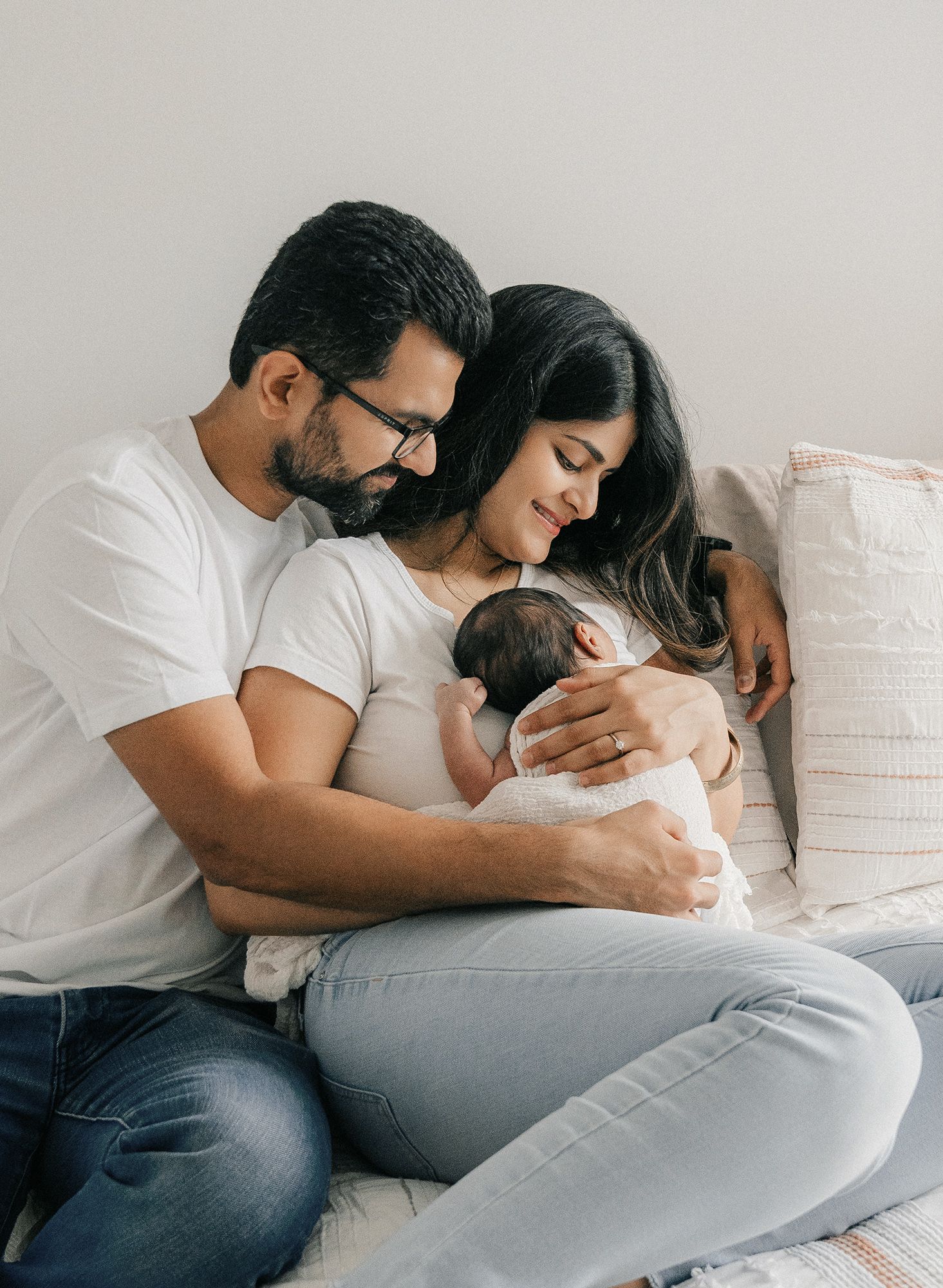 Happy couple sitting on bed together cradling their newborn baby in a tender family portrait.
