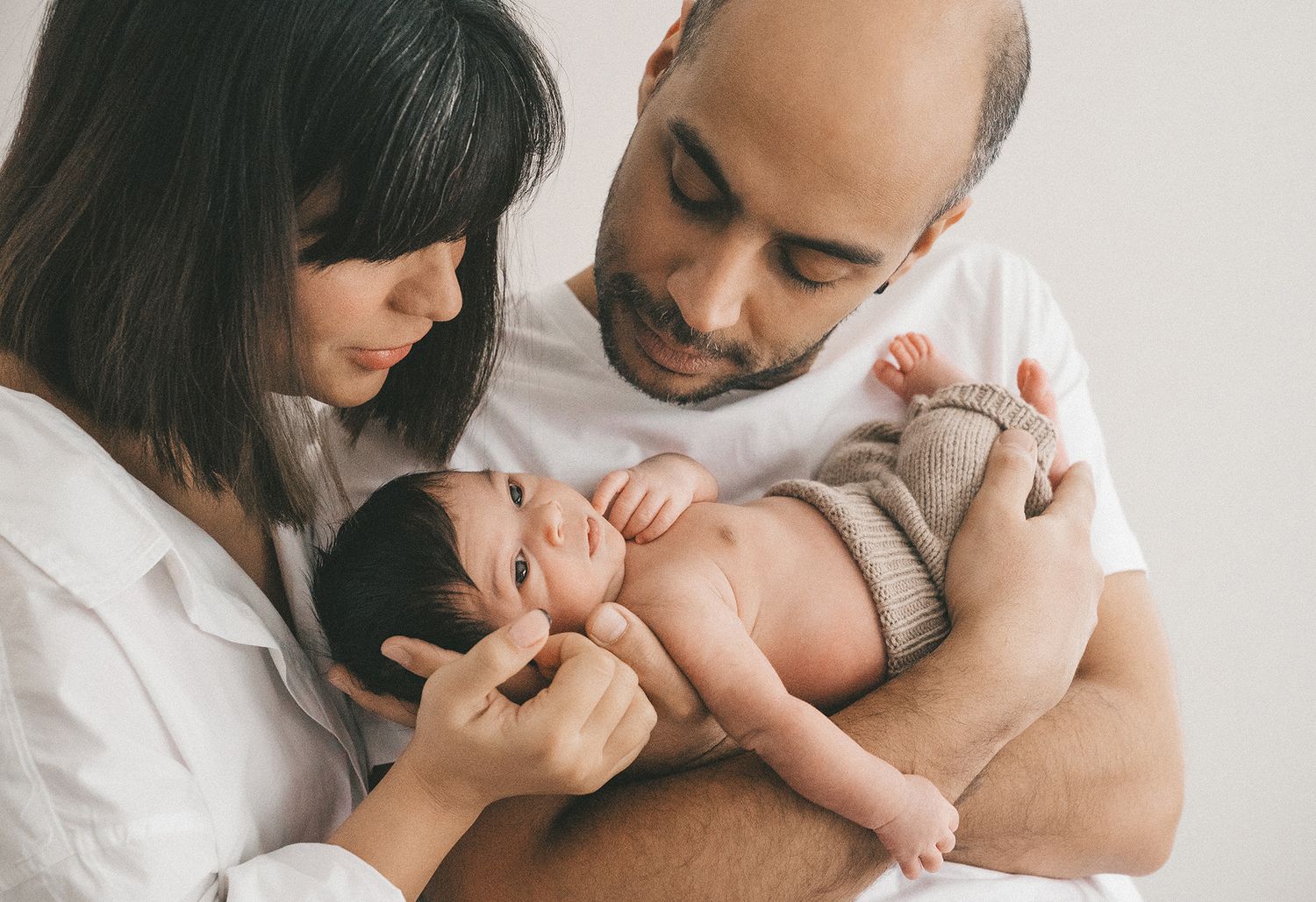 New parents lovingly holding their awake newborn baby dressed in a knit outfit.