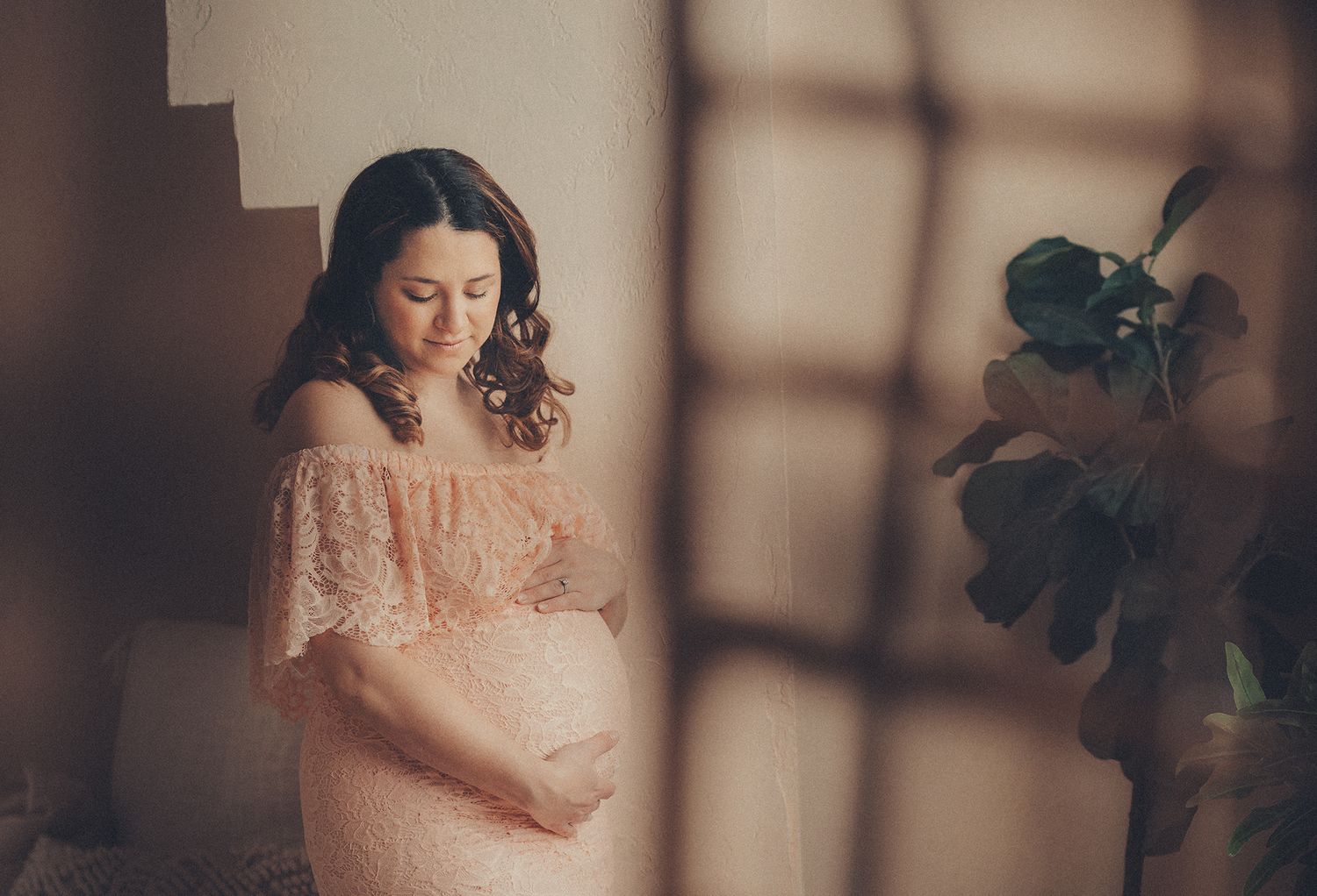 Pregnant woman in pink lace dress cradling baby bump on staircase.