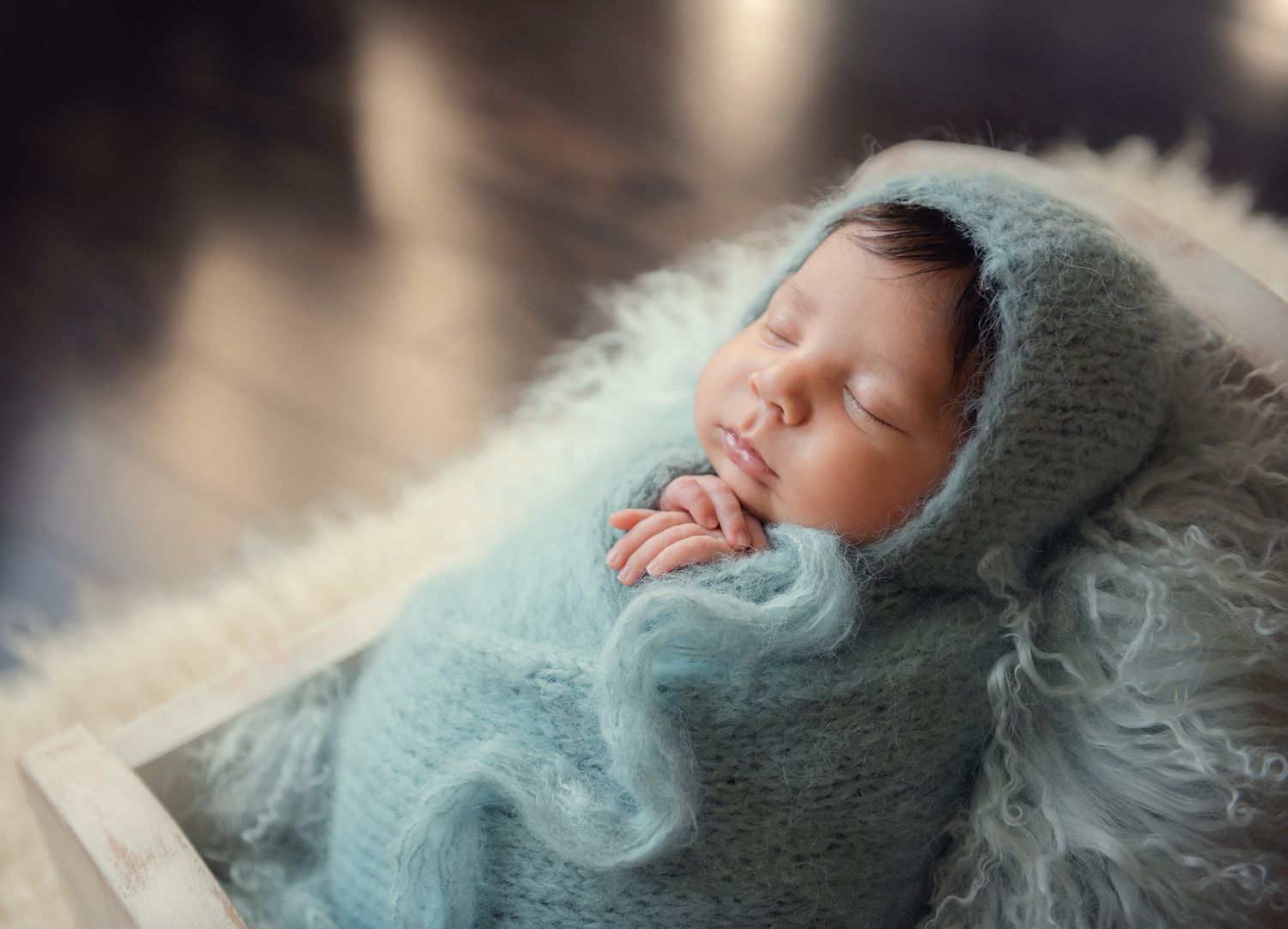 Sleeping newborn wrapped in a soft teal knit blanket and bonnet, posed in a wooden crate.