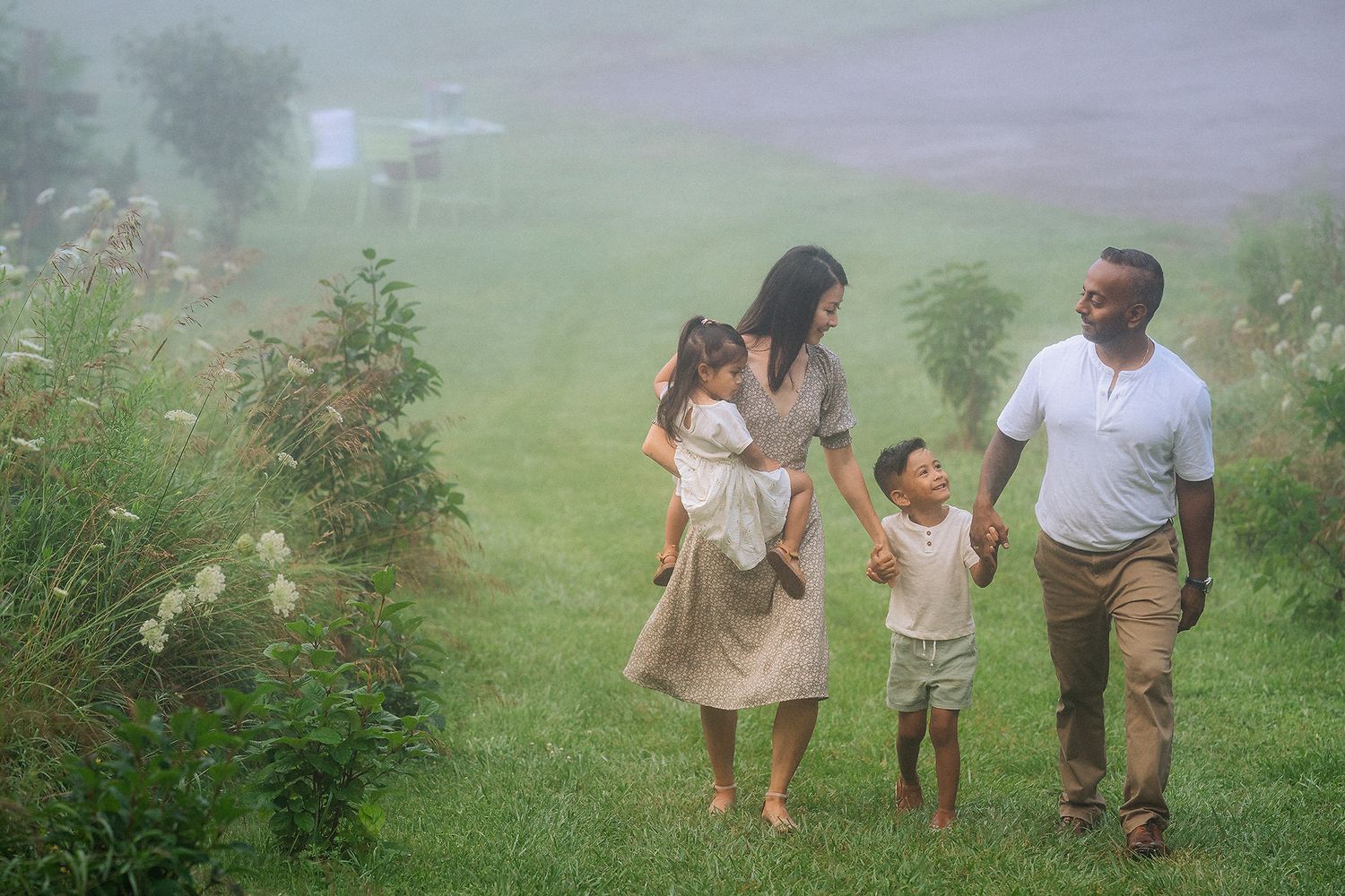 Interracial family of four walks hand in hand through a misty green meadow on a foggy day.