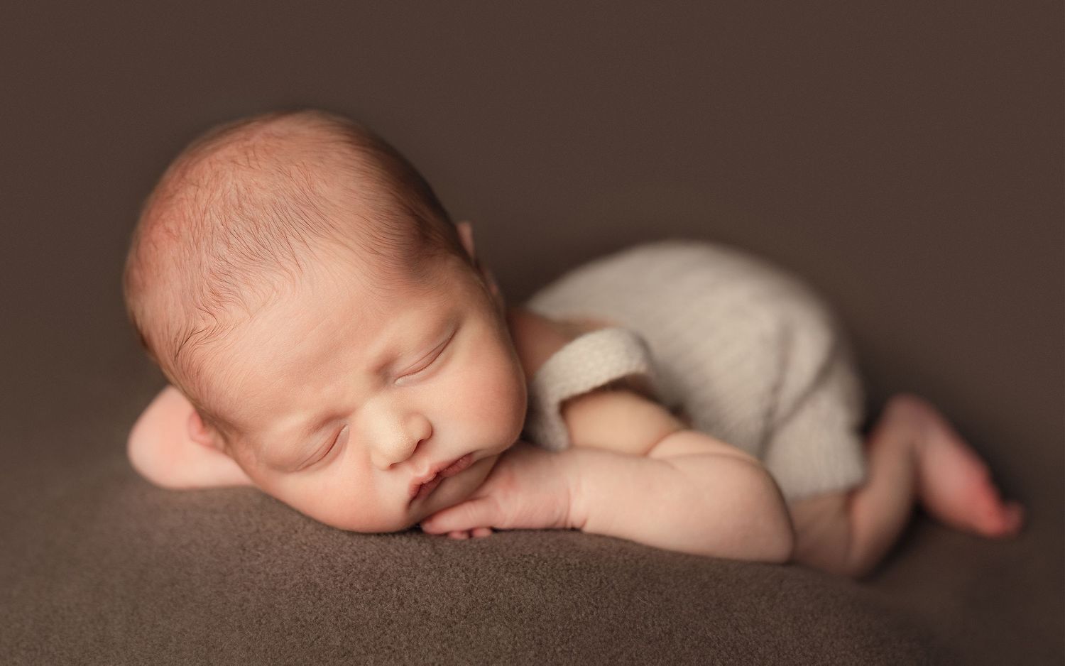 Peaceful newborn baby sleeping in fetal position on brown backdrop.