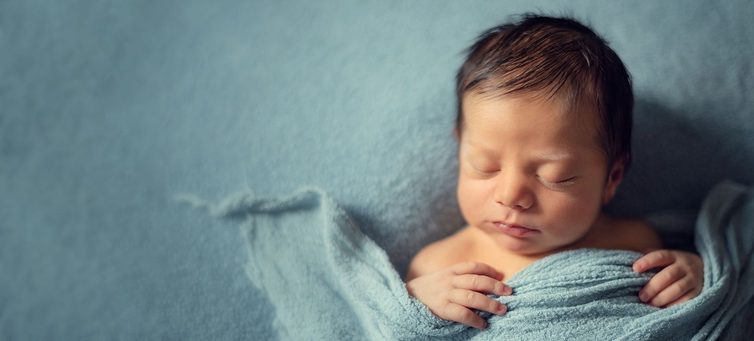 Serene newborn infant sleeping soundly swaddled in a cozy light blue wrap on a blue backdrop.
