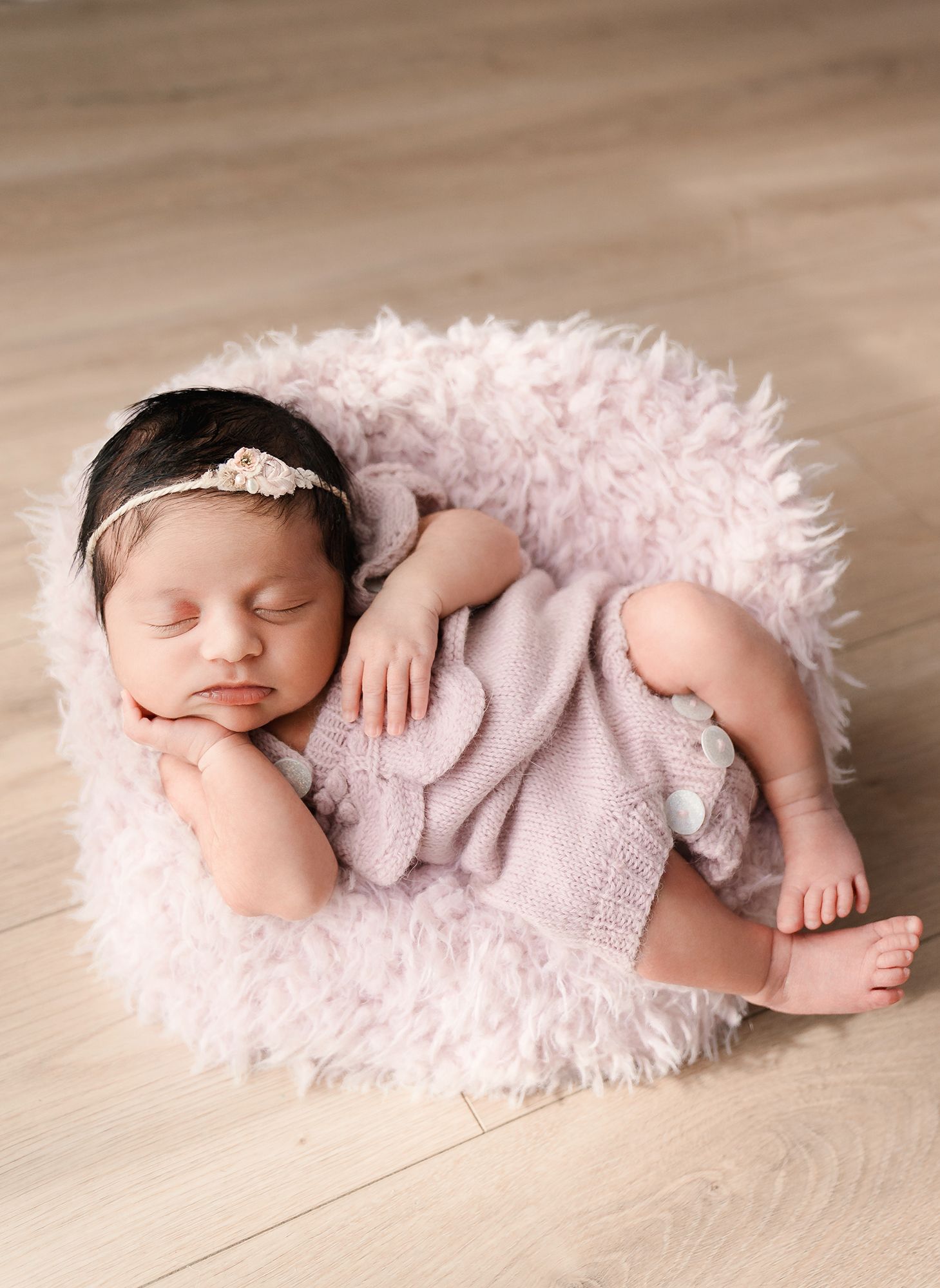 Newborn baby girl sleeping in pink knit outfit on a fluffy pink fur cushion.