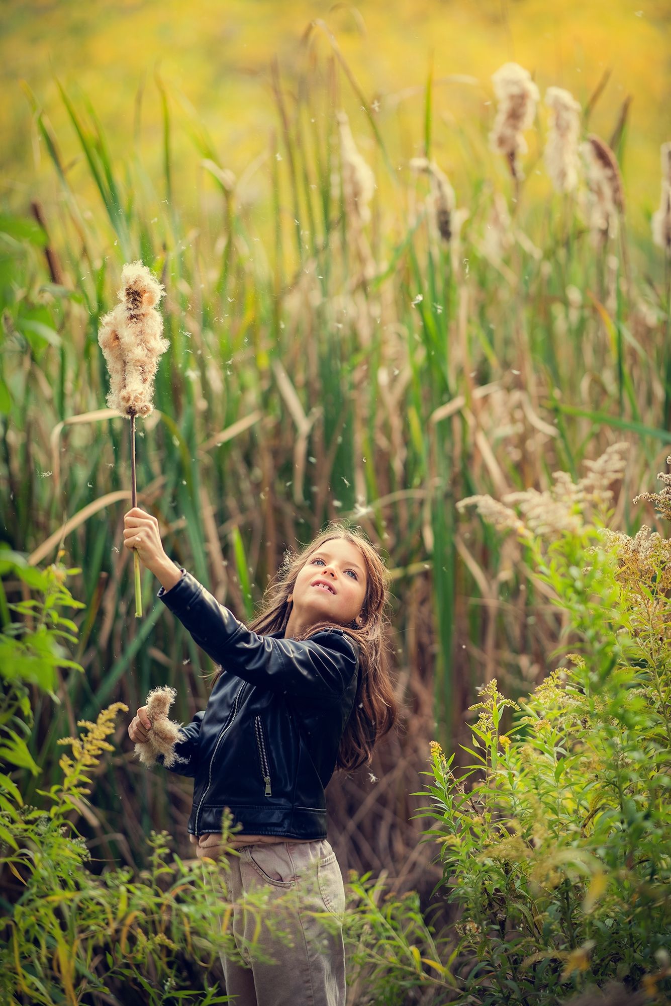 Happy girl in leather jacket playing with tall reed grass in lush green field.
