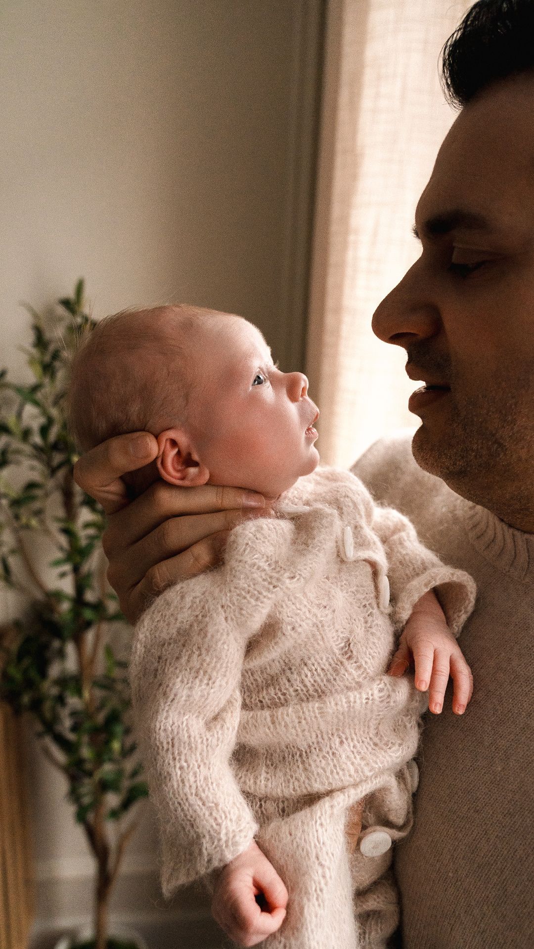 Father tenderly holding alert newborn baby in soft natural indoor lighting.