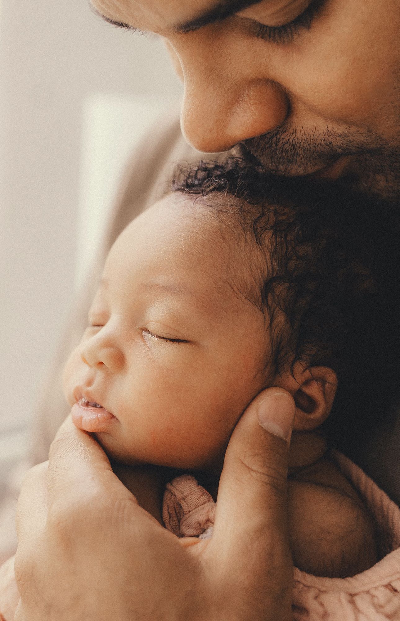 Tender moment of a father gently kissing his sleeping newborn baby held carefully in his hands.