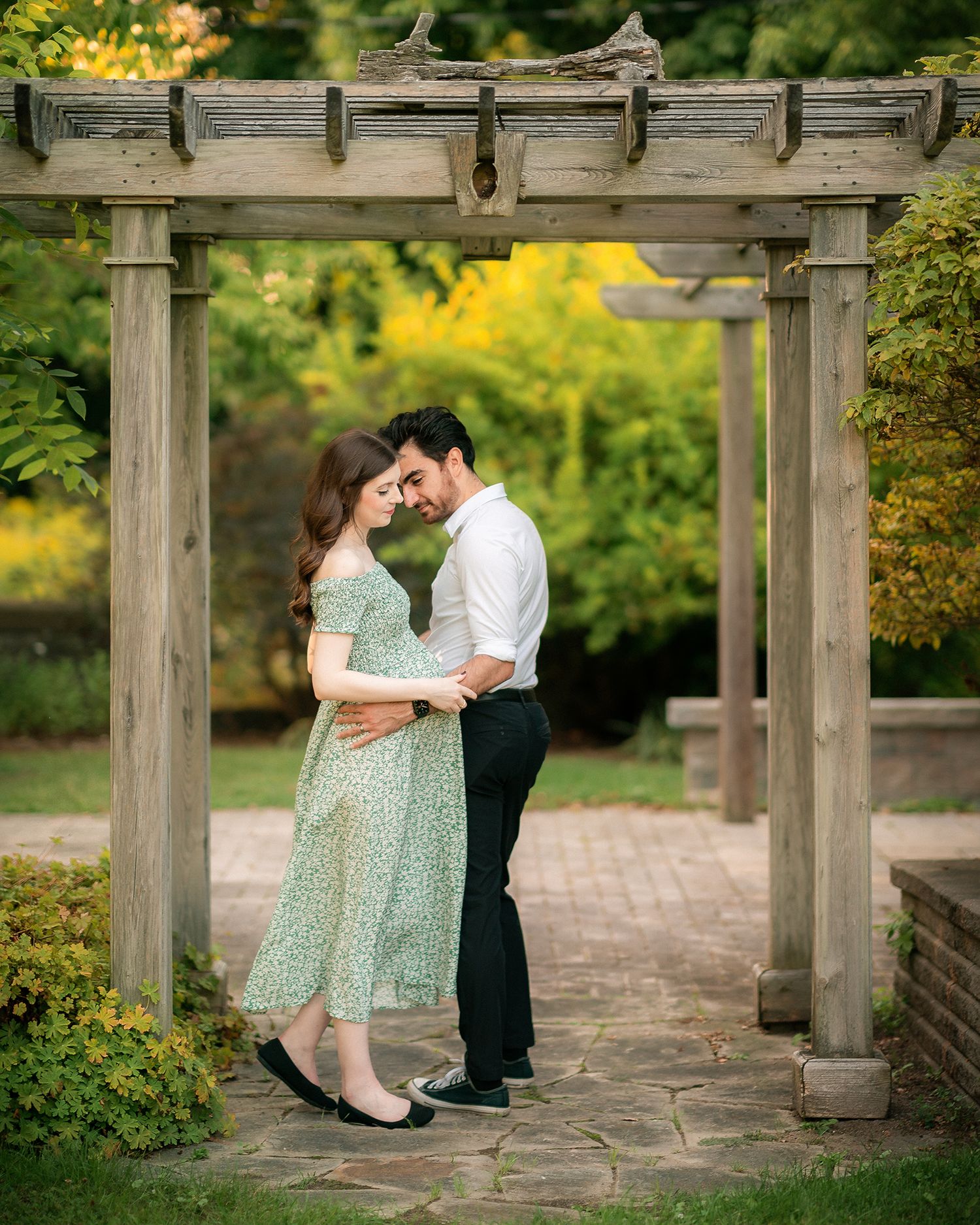 A couple shares a tender moment under a rustic wooden pergola arch in a lush green garden.
