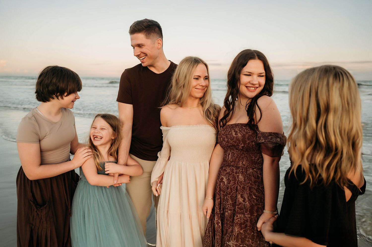 Happy family of six smiling together on beach at sunset in casual elegant outfits.