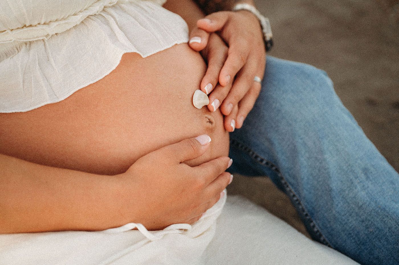 Close-up of pregnant woman's belly with partner's hands gently resting on it outdoors.