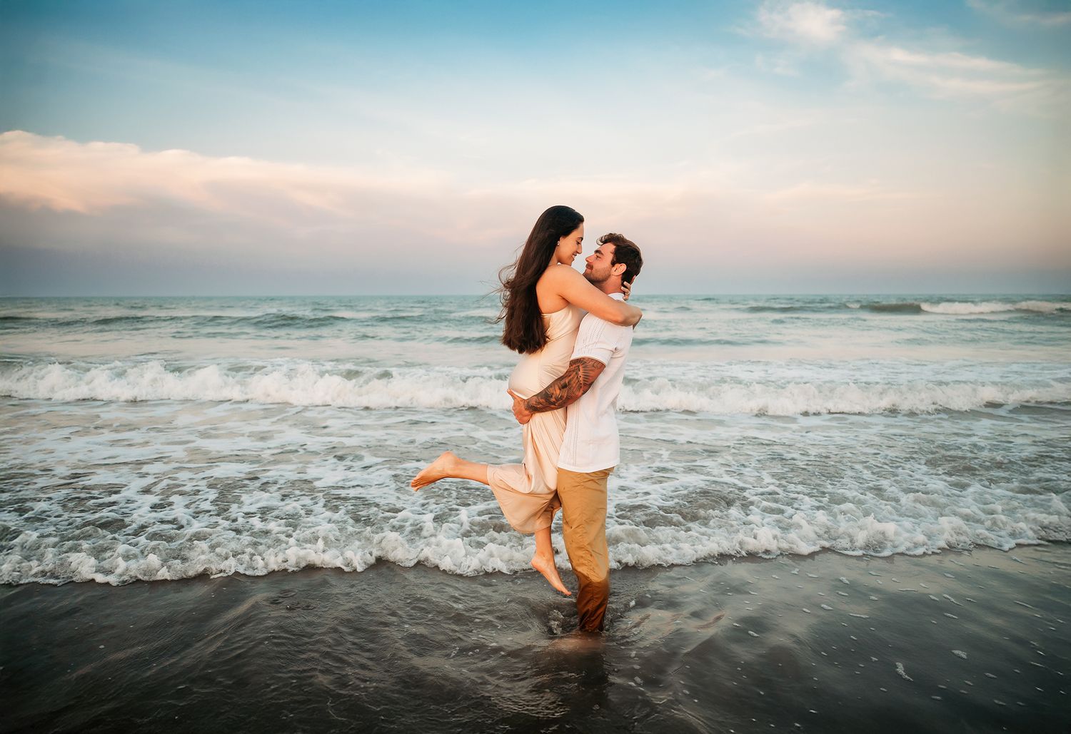 Couple embracing and kissing on a beach at sunset, waves crashing behind them on a romantic evening.