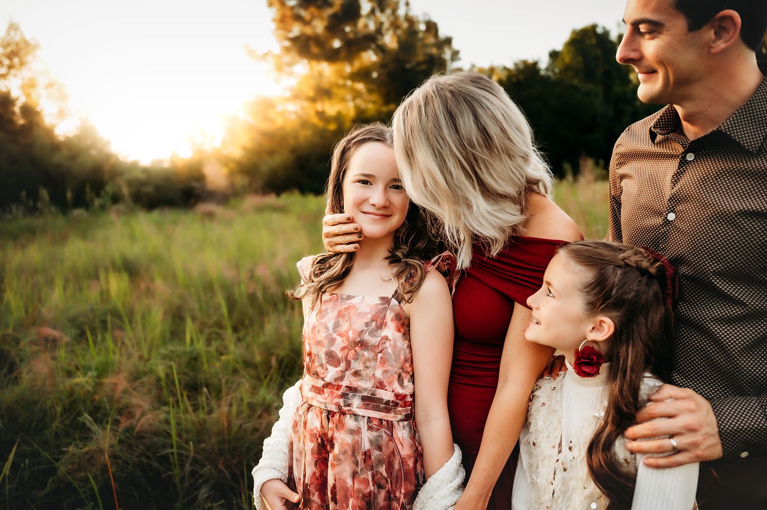 Family of four sharing a warm embrace in a sunlit meadow, with golden hour light glowing behind them.