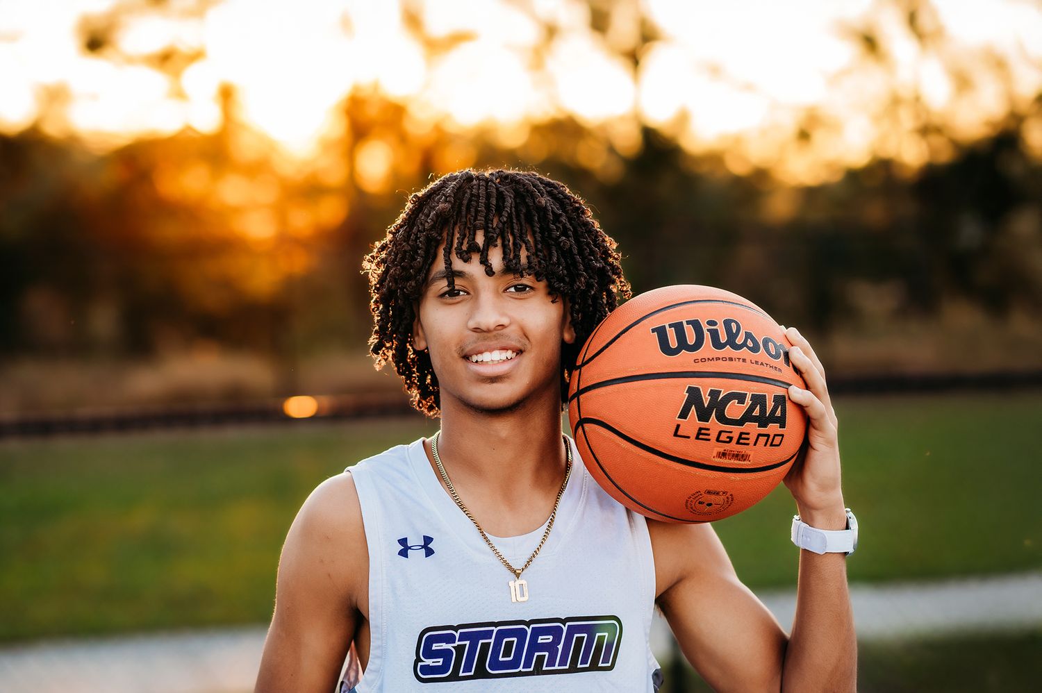 Young basketball player holding a Wilson NCAA Legend ball, wearing a Storm jersey at golden hour outdoors.