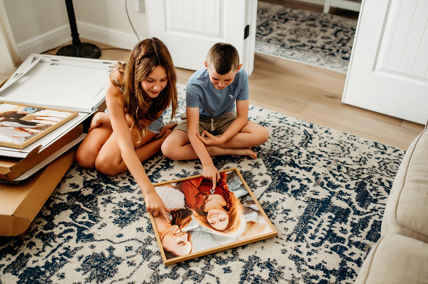 Two children sitting on patterned rug examining family photos together in bright home interior.