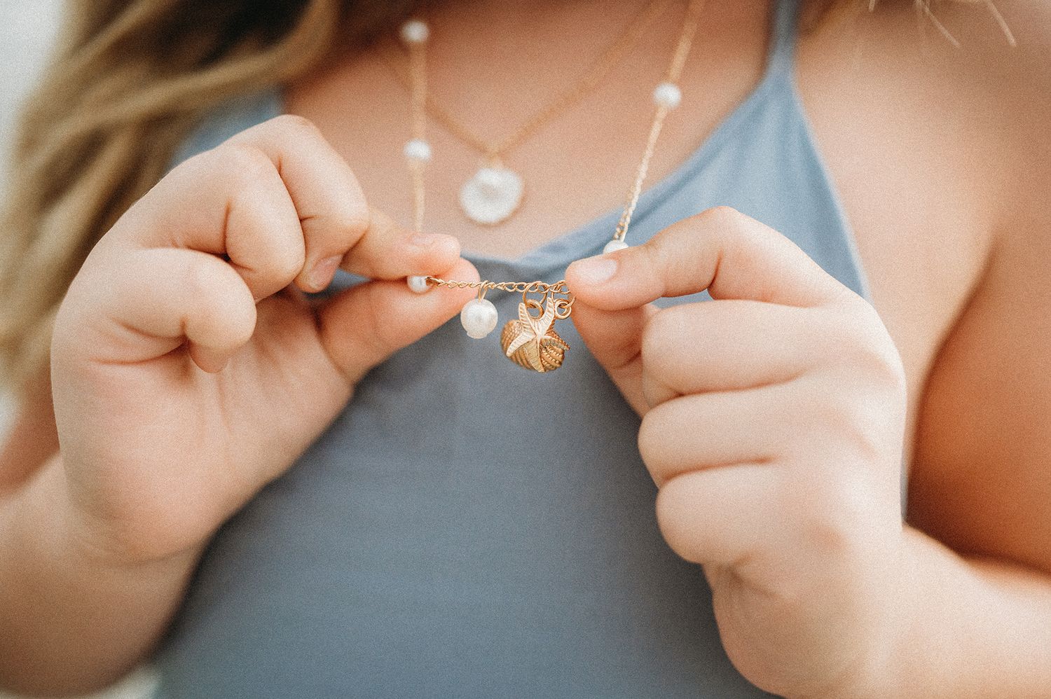 Close-up of woman holding layered necklaces with star and pearl pendants on blue top.