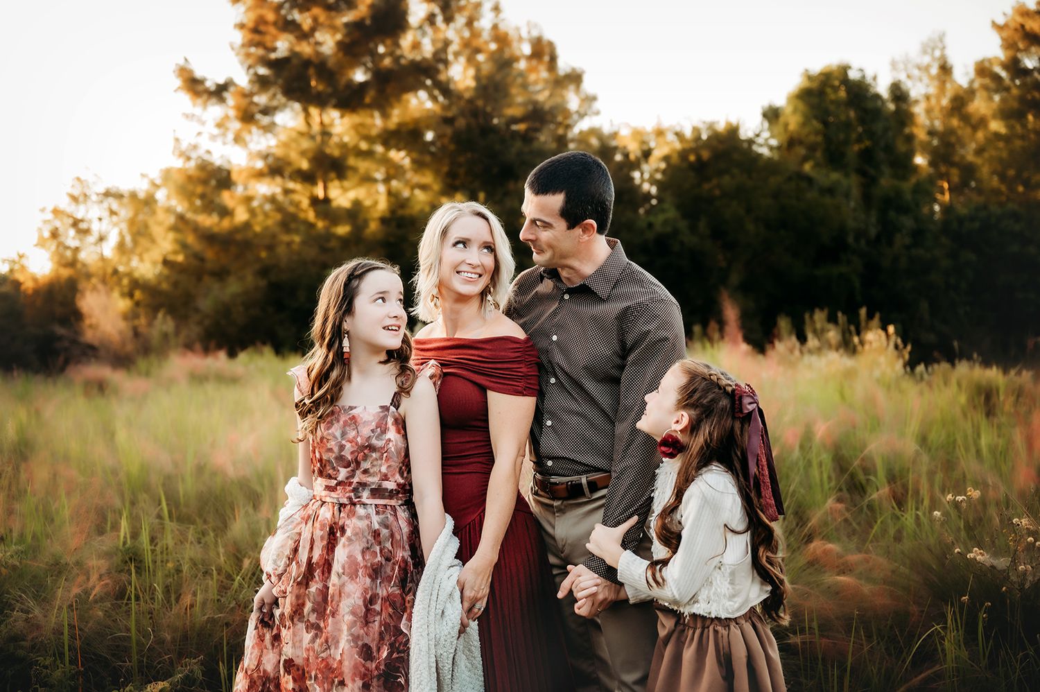 Happy family of four posing together in a sunlit meadow during golden hour outdoor photo session.