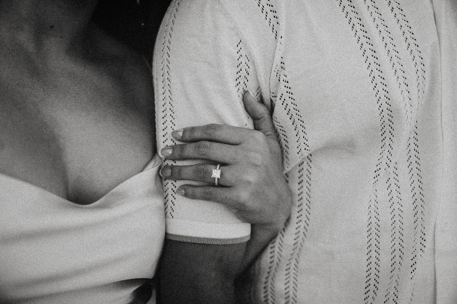 Black and white photo of a couple embracing, woman's hand with wedding ring resting on man's arm.
