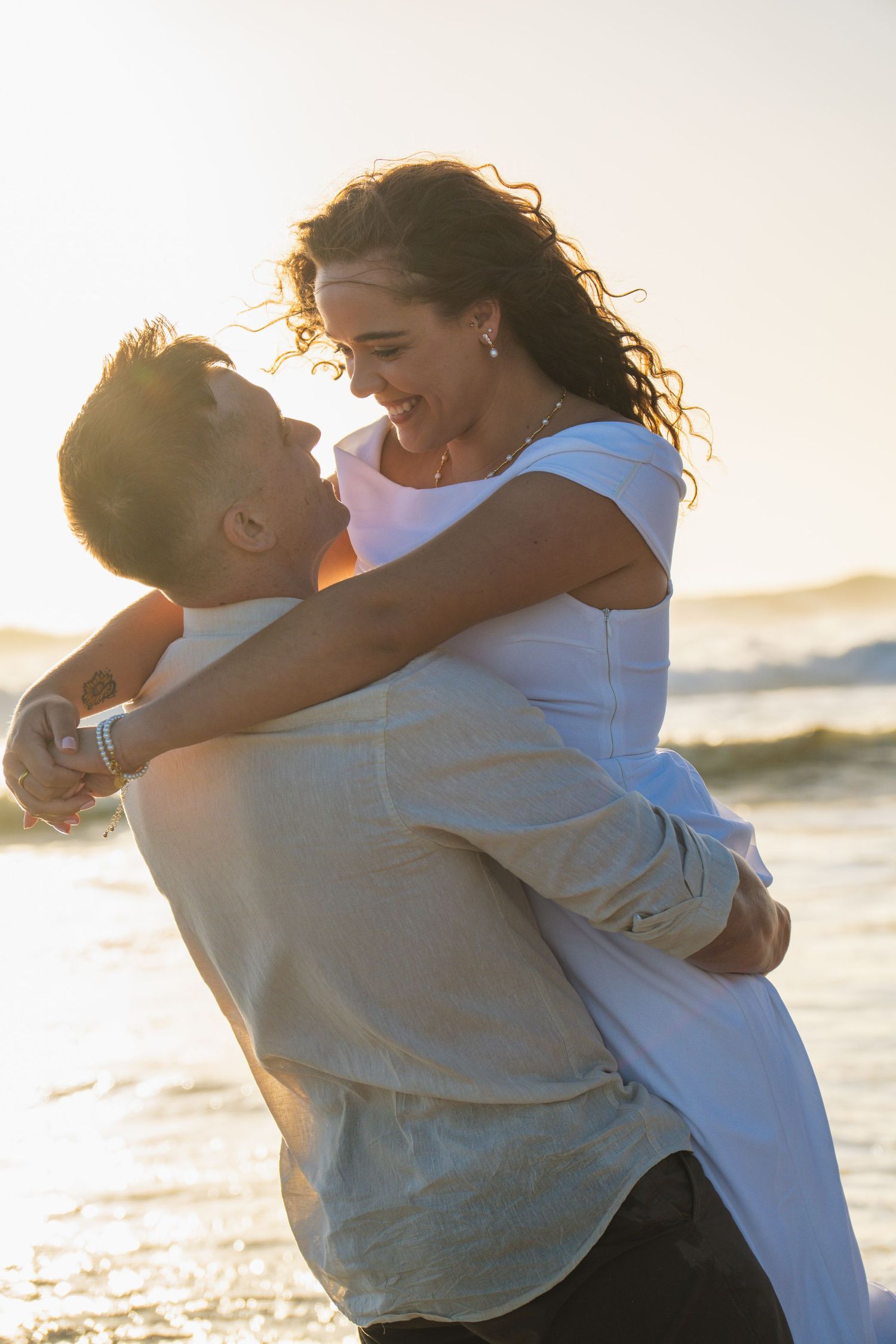 Couple laughing and embracing by the ocean at sunset during a Cape Town engagement photography session.