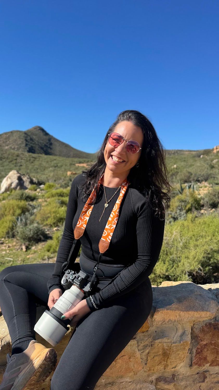 Self-portrait of Cape Town photographer Charlene Vrey outdoors with her camera against a mountain landscape.