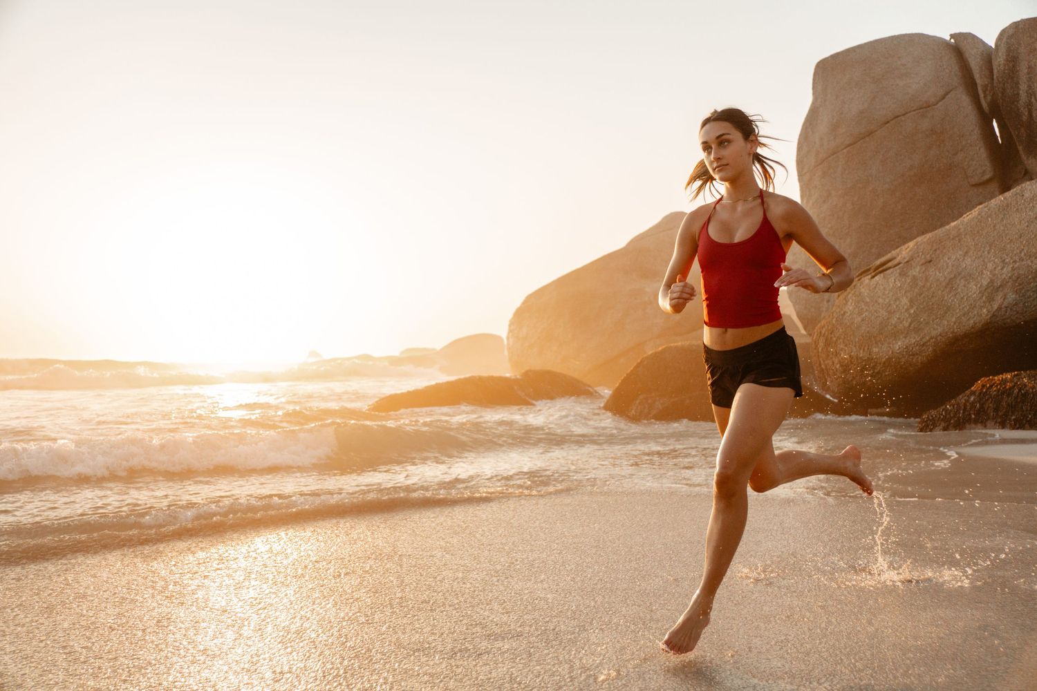 Female athlete running along a Cape Town beach at sunset, captured through outdoor fitness and lifestyle photography.