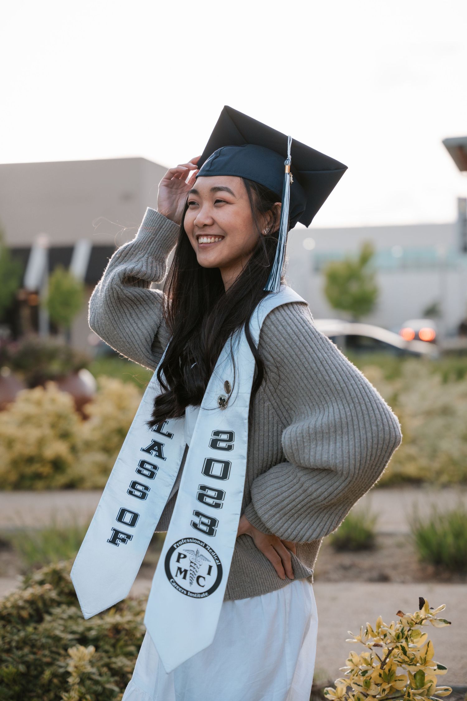 Smiling graduate in cap and Class of 2023 stole posing outdoors with hand on mortarboard.