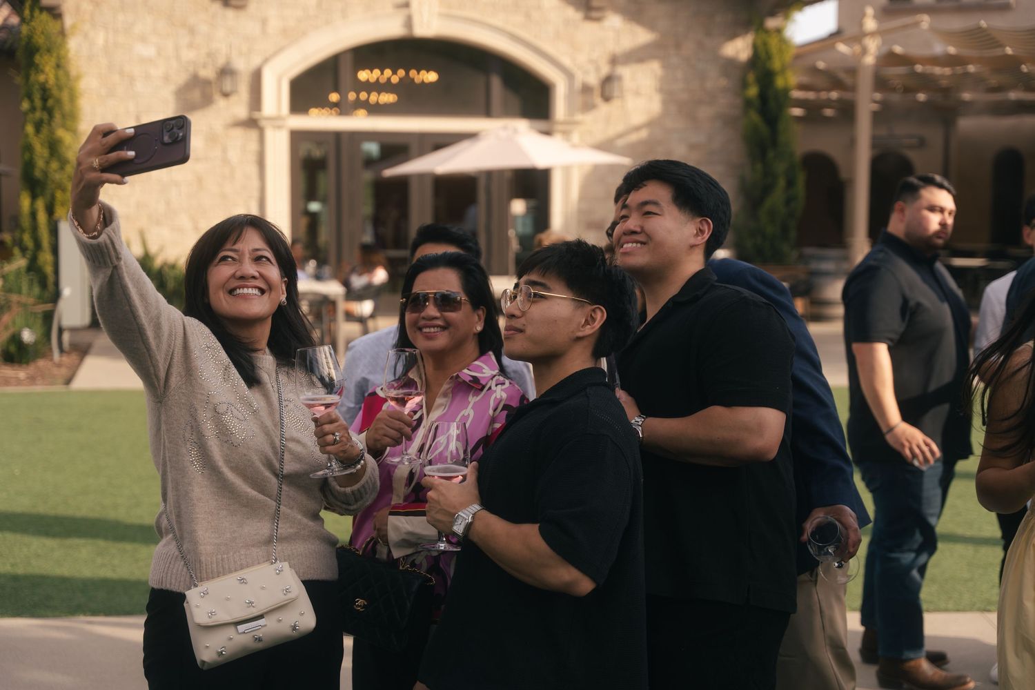 Group of four guests taking outdoor selfie with wine glasses at wedding reception.