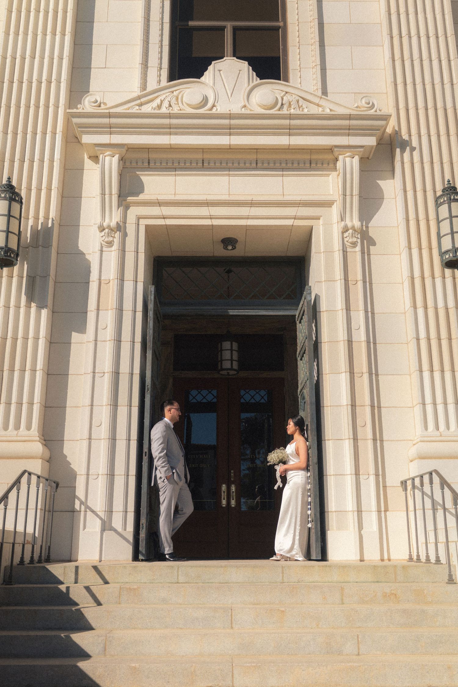 Bride and groom facing each other at the entrance of a grand neoclassical building.